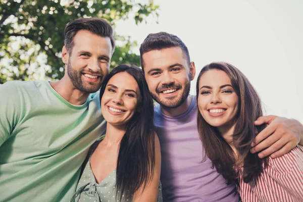 Sudut pandang yang rendah foto empat teman yang bahagia laki-laki dan perempuan berpelukan tersenyum tersenyum dengan suasana hati yang baik di luar ruangan — Stok Foto