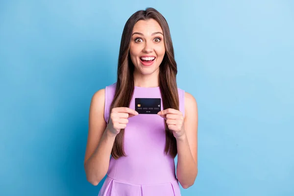 Фотографія весела збуджена дівчина в рожевій сукні, що показує банківську карту, посміхаючись, ізольована на яскравому синьому кольоровому фоні — стокове фото