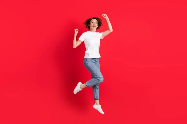Πλήρες μήκος του σώματος άποψη του μεγέθους ελκυστική χαρούμενη κοκαλιάρικο κορίτσι άλμα χαρά απομονωμένη πάνω από φωτεινό φόντο κόκκινο χρώμα — Φωτογραφία Αρχείου
