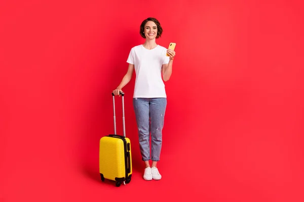 Tamanho do corpo de comprimento total vista de menina alegre atraente usando gadget segurando saco ordem de táxi isolado sobre fundo de cor vermelha brilhante — Fotografia de Stock