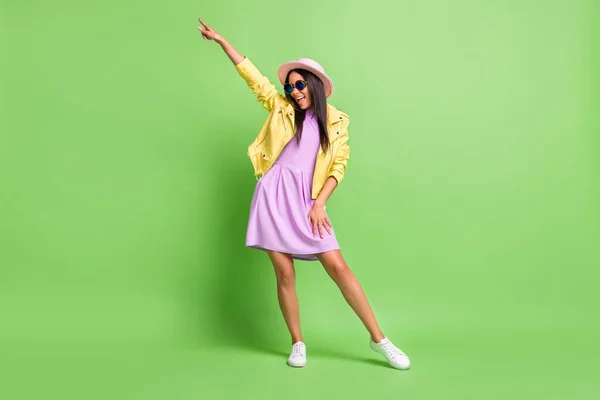 Φωτογραφία από χαριτωμένο αστείο κορίτσι χαίρονται funky χορό φορούν κίτρινο σακάκι μοβ φόρεμα ροζ καπέλο υποδήματα απομονωμένο πράσινο χρώμα φόντο — Φωτογραφία Αρχείου