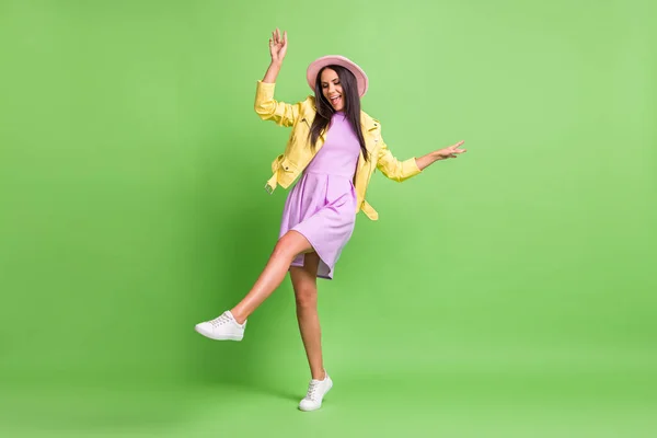 Foto de chica encantadora despreocupada disfrutar de danza usar chaqueta amarilla vestido violeta sombrero rosa calzado aislado color verde fondo — Foto de Stock