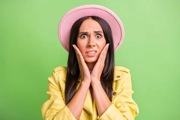 Foto retrato de mulher nervosa estressada tocando as maçãs do rosto mãos olhando em chapéu rosa isolado no fundo cor verde vibrante — Fotografia de Stock