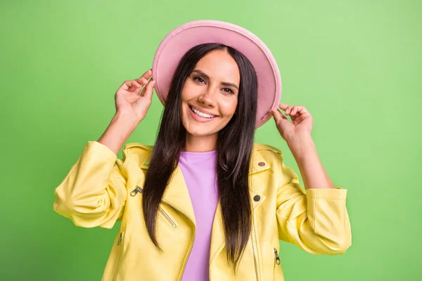 Foto retrato de menina morena vestindo roupa de outono sorrindo tocando chapéu ambas as mãos isoladas no fundo de cor verde brilhante — Fotografia de Stock