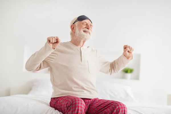Фото пожилого сонного человека счастливая положительная улыбка сидеть на кровати дома растягивая проснуться носить пижаму глаза маску — стоковое фото