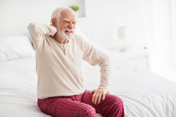 老年人养老金领取者坐在被窝里不高兴、伤心、烦躁、手摸肩膀疼痛痉挛的照片 — 图库照片