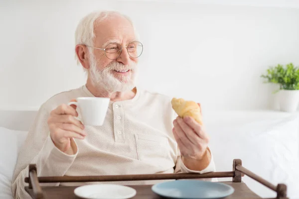 高齢者の写真幸せな肯定的な笑顔の夢を見て空のスペースはベッドの上で朝食を持ってコーヒーを飲むクロワッサン家を食べる — ストック写真