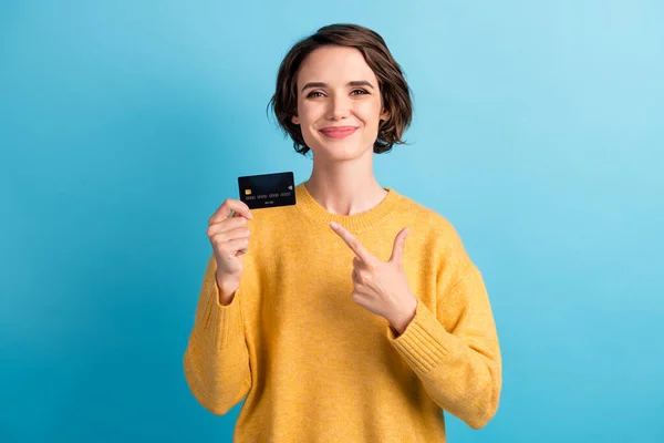 Retrato de adorável doce jovem bob penteado senhora apontando cartão de banco desgaste camisola amarela isolada no fundo de cor azul brilhante — Fotografia de Stock