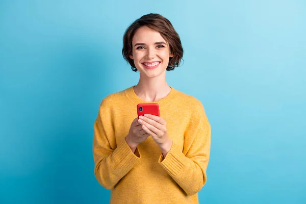 Foto de adorable dama radiante con suéter amarillo casual sosteniendo brazos manos teléfono aislado color azul fondo — Foto de Stock