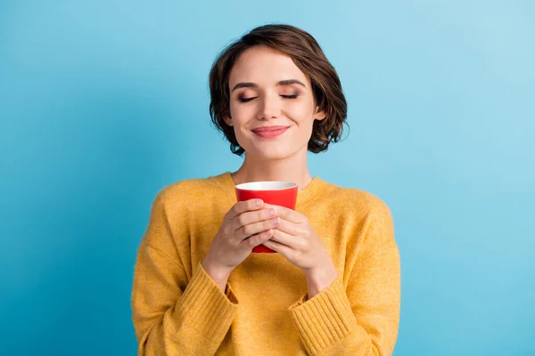 Foto de mulher doce brilhante vestido casual pulôver amarelo desfrutar de café aroma copo mãos braços isolado azul cor fundo — Fotografia de Stock