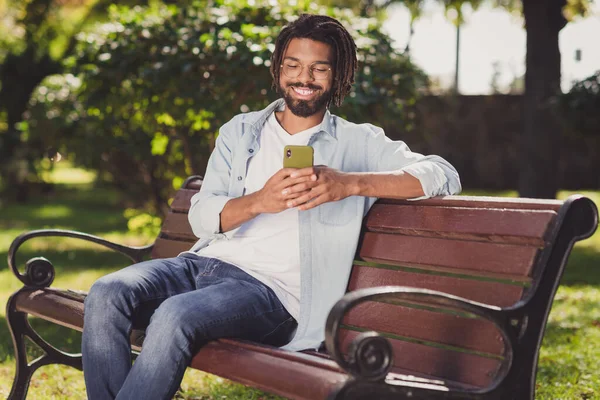 一个英俊快乐的男人坐在长椅上，用设备浏览媒体，在户外聊天的都市夏季 — 图库照片