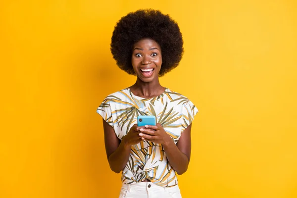 Fotografie optimistické pěkné kudrnaté vlasy dáma psaní telefon oblečení tisk t-shirt izolované přes živé žluté barvy pozadí — Stock fotografie