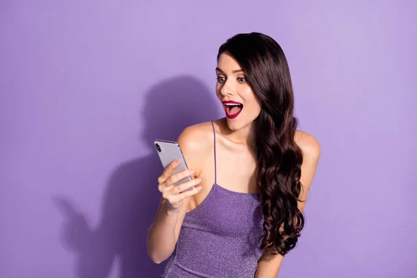 照片上年轻迷人的女孩开心的笑着惊讶的看了看被紫色背景隔开的浏览手机 — 图库照片