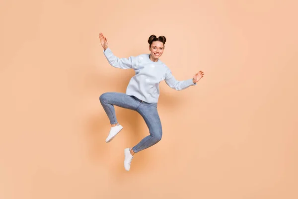 楽観的な素敵なブルネットの女性のジャンプダンスのフルサイズの写真は、ベージュの背景に隔離された青いセータージーンズスニーカーを着用 — ストック写真