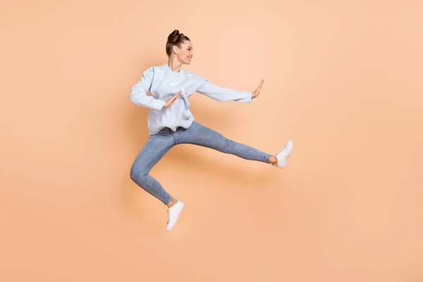 フルサイズプロフィール写真の楽観的な素敵なブルネットの女性のジャンプ空手は、ベージュの背景に隔離された青いセータージーンズスニーカーを着用 — ストック写真