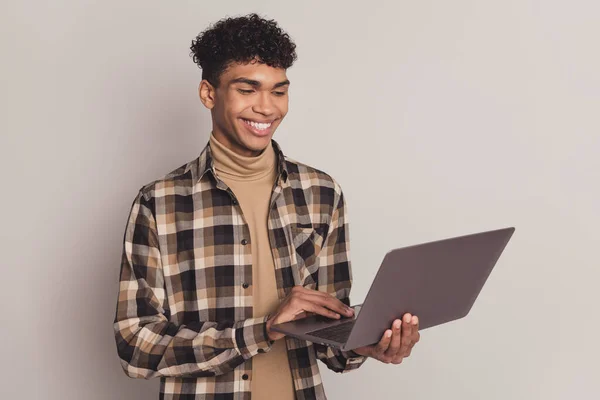 Foto retrato de un niño joven con camisa a cuadros trabajando en el ordenador portátil haciendo proyecto sonriendo aislado sobre fondo de color gris —  Fotos de Stock