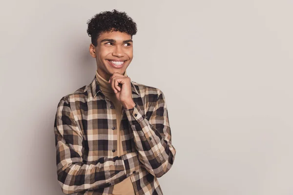 Foto di mentalità felice pelle scura giovane sguardo vuoto spazio tenere la mano mento sorriso isolato su sfondo di colore grigio — Foto Stock