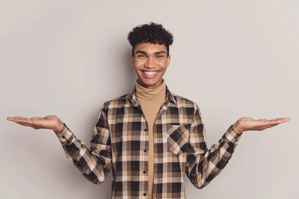 Foto av glad glad brunett stilig mörk hud kille hålla händerna tomt utrymme leende isolerad på grå färg bakgrund — Stockfoto