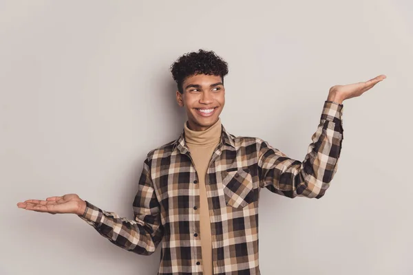 Zdjęcie portret młodego chłopca w koszuli w kratę uśmiechnięty porównując puste przestrzenie na rękach ciekawy izolowany na szarym tle koloru — Zdjęcie stockowe