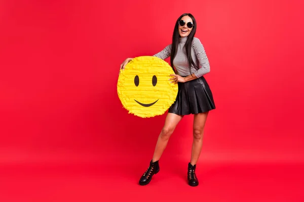 Foto de tamaño completo de la joven alegre positiva sostener papel sonrisa piñata emoji buen humor aislado sobre fondo de color rojo —  Fotos de Stock
