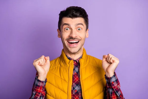 Foto de divertido afortunado joven usar chaqueta amarilla sin mangas levantando puños aislados color violeta fondo — Foto de Stock