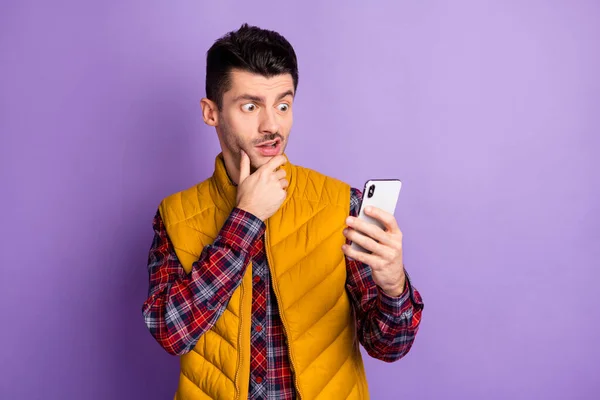 Фото красивый шокированный молодой человек держит взгляд смартфон думаю, пост изолирован на фиолетовом фоне цвета — стоковое фото