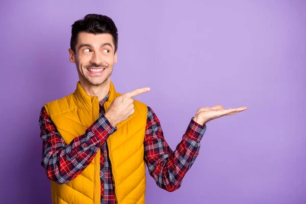 Foto di carino uomo affascinante indossare giacca gialla senza maniche guardando puntando braccio spazio vuoto isolato colore viola sfondo — Foto Stock