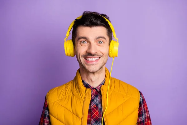 Fénykép a bájos pozitív fiatalember viselni sárga ujjatlan kabát fejhallgató mosolygó elszigetelt ibolya színű háttér — Stock Fotó