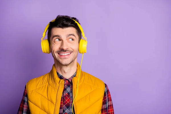 Foto von positiven jungen Mann tragen gelbe ärmellose Jacke Kopfhörer suchen leeren Raum isoliert violette Farbe Hintergrund — Stockfoto