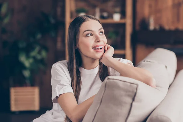 Foto de adorable mujer joven soñadora camiseta blanca sentado sofá brazo mejilla mirando ventana sonriendo interior apartamento habitación — Foto de Stock