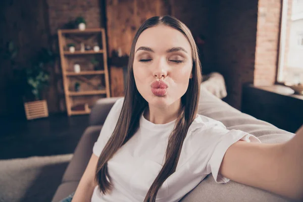 Foto van glanzende flirterige jonge dame dragen witte t-shirt zitbank opname video verzenden kus binnen huiskamer — Stockfoto
