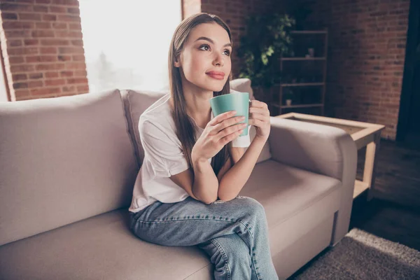 Foto de la joven soñadora brillante usar camiseta blanca sofá sentado beber bebidas en el interior habitación de la casa — Foto de Stock