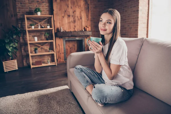 Foto van dromerige charmante jongedame dragen witte t-shirt zitbank drinken thee met rust binnen huiskamer — Stockfoto