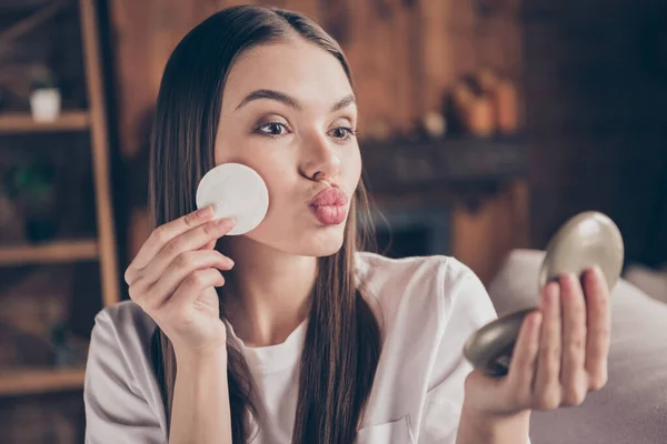 Photo of shiny beautiful young lady wear white t-shirt sitting sofa applying makeup sending mirror kiss indoors house room