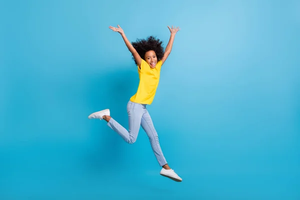 Perfil de corpo inteiro foto lateral afro-americano volume cabelo menina desgaste jeans amarelo t-shirt levantar as mãos salto isolado no fundo de cor azul — Fotografia de Stock
