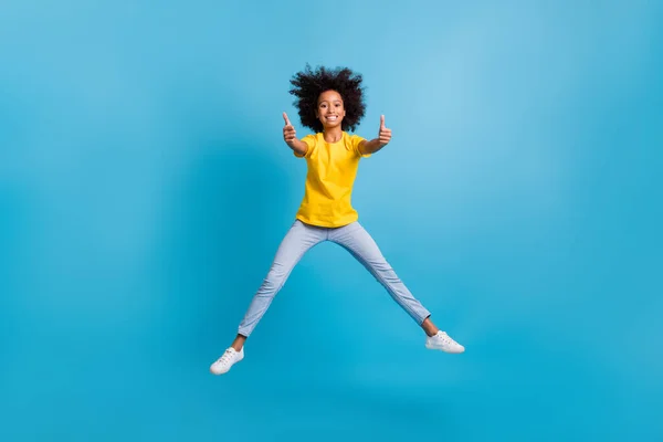 Full body photo of brown haired dark skin little girl jump up show thumbs up wear casual outfit isolated on blue color background — Stock Photo, Image