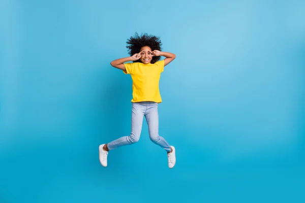 Фотографія повного тіла темної шкіри брюнетки маленька дівчинка робить v-знаки стрибати носити жовті футболки джинси ізольовані на синьому кольорі — стокове фото