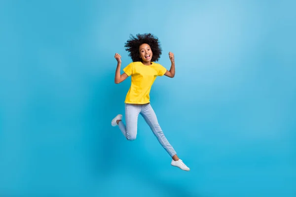 Foto em tamanho completo de afro americano na moda morena menina salto ganhar desgaste amarelo t-shirt jeans isolado no fundo de cor azul — Fotografia de Stock