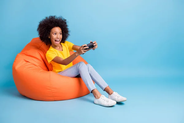 Lunghezza completa foto di pelle scura bruna ragazza gioco joystick sit bean bag usura giallo t-shirt isolato su sfondo di colore blu — Foto Stock