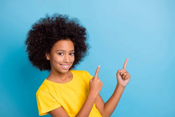 Photo of nice dark skin brunette girl point fingers empty space wear yellow t-shirt isolated on blue color background — Stock Photo, Image