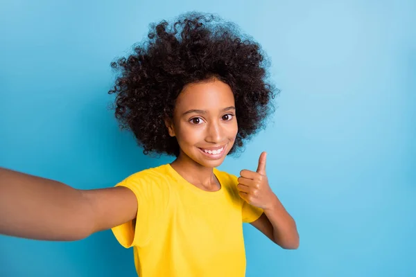 Esmer, küçük Afro-Amerikalı kızın sarı tişört giydiği fotoğraf. Selfie çek. Mavi arka planda izole edilmiş bir parmak yap. — Stok fotoğraf