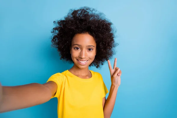 Foto di bruna piccola pelle scura positiva ragazza indossare giallo t-shirt fare selfie v-segno isolato su sfondo di colore blu — Foto Stock