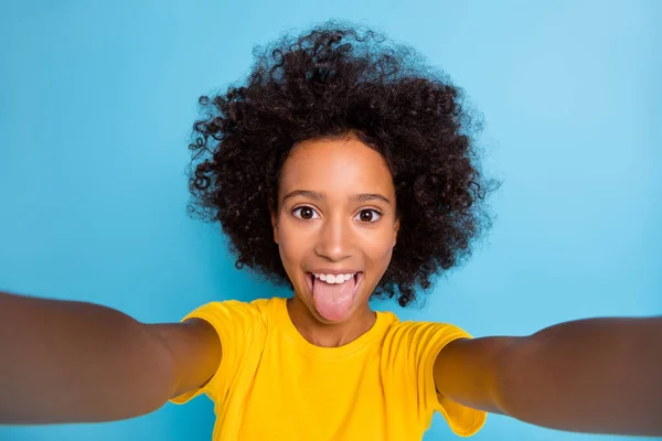 Foto divertente pelle scura marrone bambina dai capelli indossare giallo t-shirt prendere selfie ingannare faccia isolata su sfondo di colore blu — Foto Stock