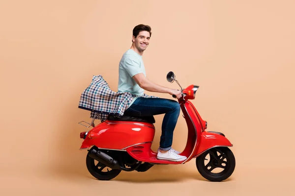 Profil sisi tampilan potret menarik ceria pria mengemudi merah moped menghabiskan waktu jalan tur terisolasi atas warna latar beige pastel — Stok Foto