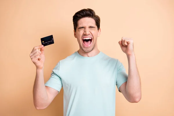 Portret van mooie gelukkige vrolijke man houden in de hand bankkaart vieren succes hebben plezier geïsoleerd over beige pastel kleur achtergrond — Stockfoto