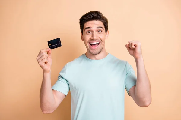 Portret van mooie vrolijke man in de hand bank kaart vieren lening storting succes geïsoleerd over beige pastel kleur achtergrond — Stockfoto