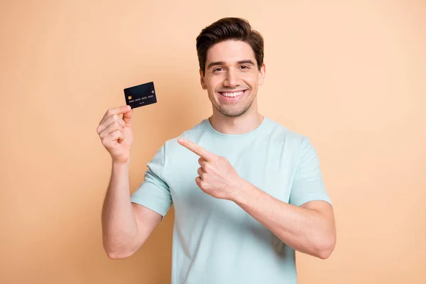 Portret van een leuke vrolijke man met behulp van holding in de hand demonstreren bankkaart oplossing geïsoleerd over beige pastel kleur achtergrond — Stockfoto