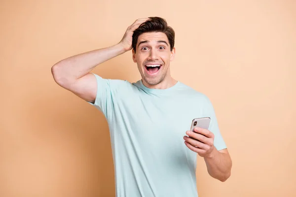 Portret van mooie vrolijke verbaasd guy influenzer met behulp van apparaat browsen media nieuws smm geïsoleerd over beige pastel kleur achtergrond — Stockfoto