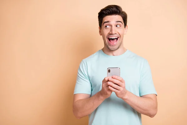 Retrato de agradable blogger chico sorprendido alegre usando gadget mirando a un lado anuncio de espacio de copia aislado sobre fondo de color pastel beige — Foto de Stock
