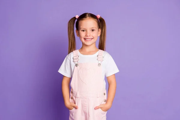 Foto de alegre menina feliz segurar mãos bolsos rosa roupa geral isolado no fundo cor violeta — Fotografia de Stock